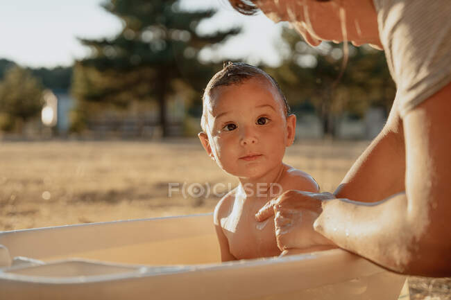 Corte irreconhecível mãe banho criança enquanto sentado no prado sob céu brilhante no dia ensolarado — Fotografia de Stock