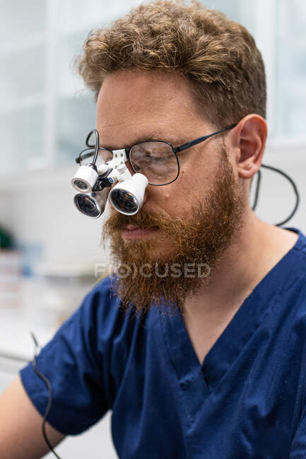 Tierarzt mit nicht gepflegtem Bart operiert mit Lupe auf Brille — Stockfoto