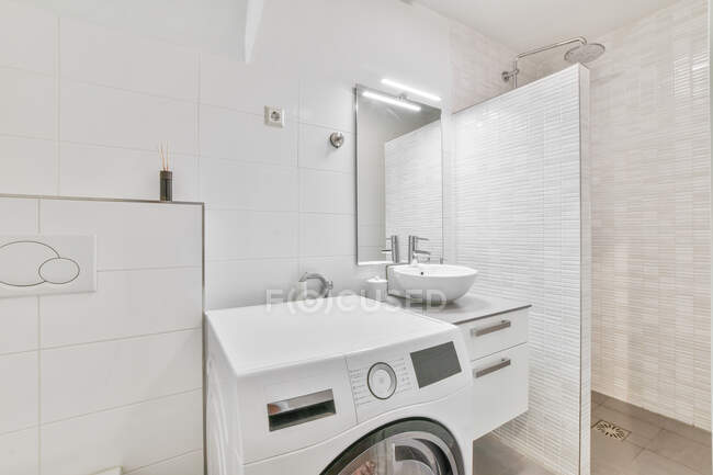 Interior do banheiro leve com máquina de lavar roupa moderna colocada perto da pia e espelho no banheiro do apartamento com cabine de chuveiro — Fotografia de Stock