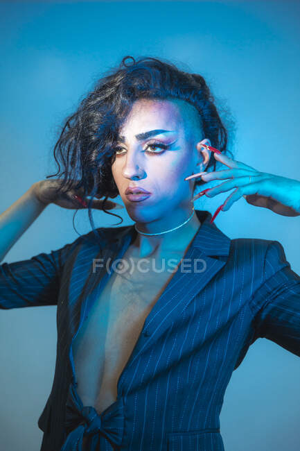 Young transsexual male model with makeup in stylish jacket looking away on blue background — Stock Photo