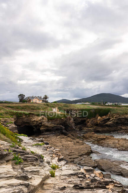 Scenery view of rough shore against mountain with residential building under shiny cloudy sky in sunlight — Stock Photo