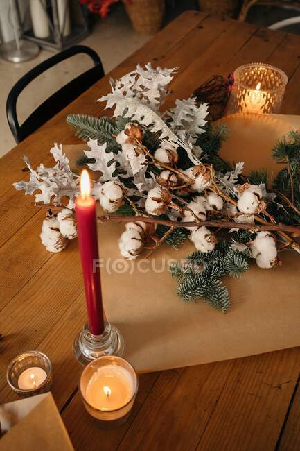 Святковий різдвяний букет з гілками бавовни і ялиці, розміщений на дерев'яному столі зі свічками в кімнаті — стокове фото