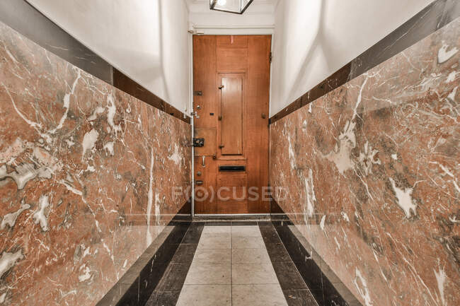 Vista panorámica del interior del pasillo largo con paredes de baldosas y piso y puerta de madera en apartamento - foto de stock