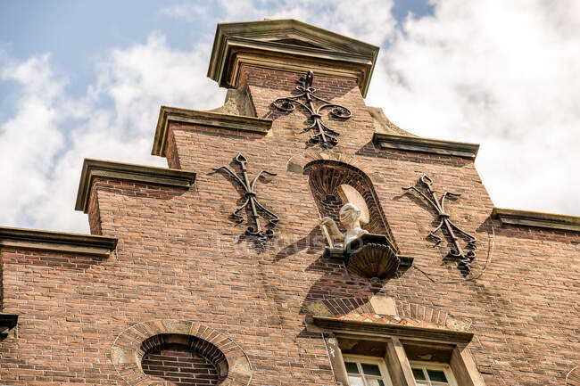 Von unten gealtertes Mauerwerk mit Skulptur und geschmiedeter Dekoration unter wolkenverhangenem Himmel in Amsterdam — Stockfoto