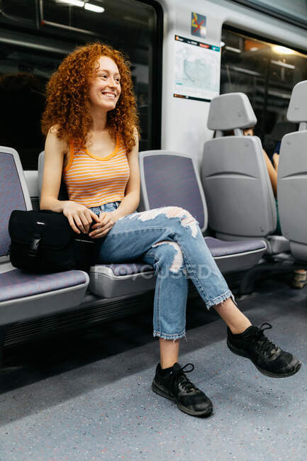 Contenu jeune femme en jeans déchiré aux cheveux roux bouclés voyageant en train — Photo de stock