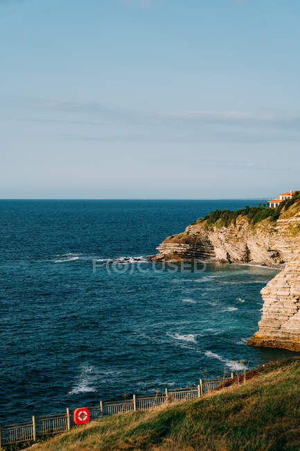 Сценический вид скалы на волнистое море с пеной и горизонтом под облачным голубым небом в Сен-Жан-де-Люз — стоковое фото