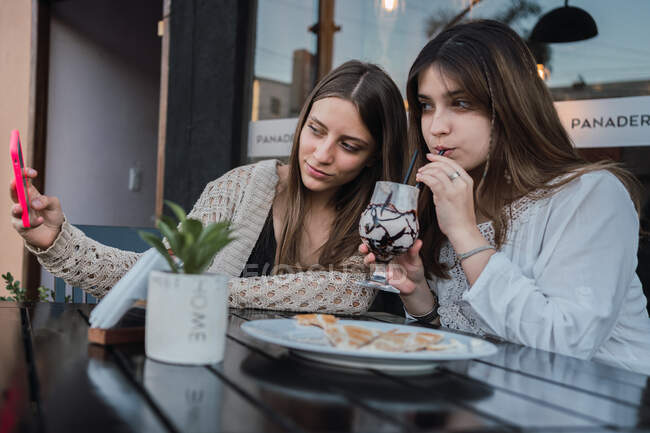 Beste Freundinnen mit Gläsern Erfrischungsgetränken beim Selbstporträt auf dem Handy am Tisch im Stadtcafé — Stockfoto