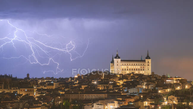 Paisaje urbano con castillo famoso envejecido Alcázar de Toledo colocado en España bajo el cielo nublado por la noche durante la tormenta - foto de stock