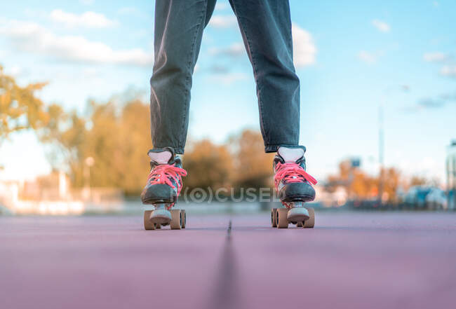 Cropped unrecognizable female wearing light pink hoodie and black jeans and roller skates with neon pink shoelaces standing in skate park — Stock Photo