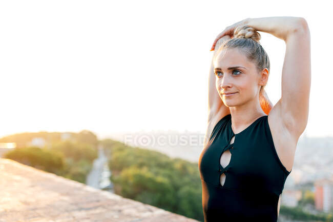 Vestibilità femminile in abbigliamento sportivo che allunga le braccia durante la pratica dello yoga sul tetto dell'edificio al tramonto — Foto stock