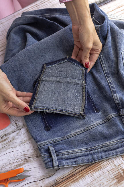 Зверху врожаю невизначена жінка з манікюром, що фіксує кишеню джинсів на столі у світлій кімнаті — стокове фото