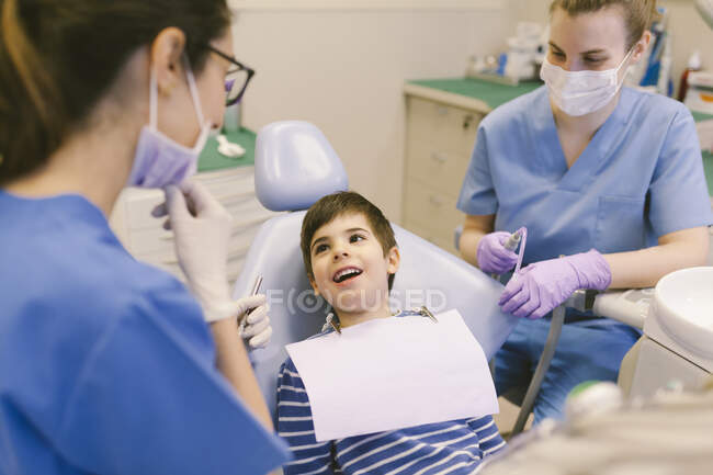 Високий кут хлопчика з ротом відкрив розмову з лікарями під час стоматологічного лікування в сучасному стоматологічному кабінеті — стокове фото