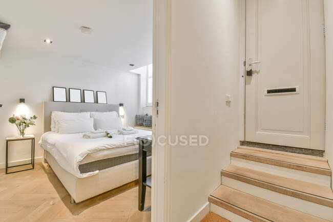 Camera da letto contemporanea con letto e lampade lucide contro parete e scala sotto porta in hotel — Foto stock