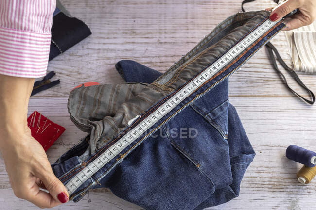 Angle élevé de la couturière femelle anonyme de culture mesurant la taille du jean sur une table en bois le jour — Photo de stock