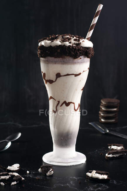 Tasty milkshake with crushed biscuits and straw in glass with chocolate sauce — Stock Photo