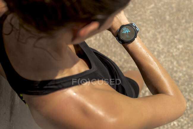 From above of crop anonymous sweaty female runner checking pulse on fitness tracker during workout on sunny day in summer — Stock Photo