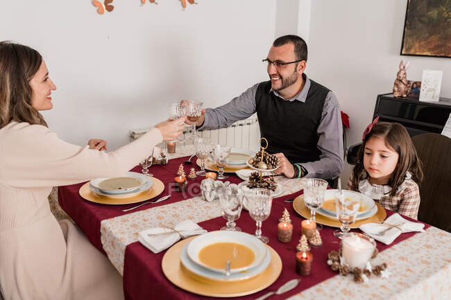 Улыбающаяся пара с декоративными стаканами алкогольного напитка над подаваемым столом с горящими свечами в Рождество дома — стоковое фото