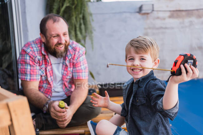 Content child having fun with measuring tape against bearded dad while spending time in daytime — Stock Photo
