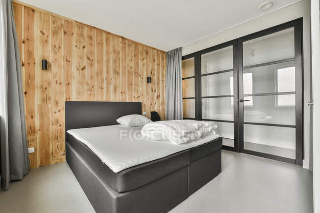 Lit confortable avec du linge blanc placé contre un mur en bois dans la chambre avec un design minimaliste — Photo de stock