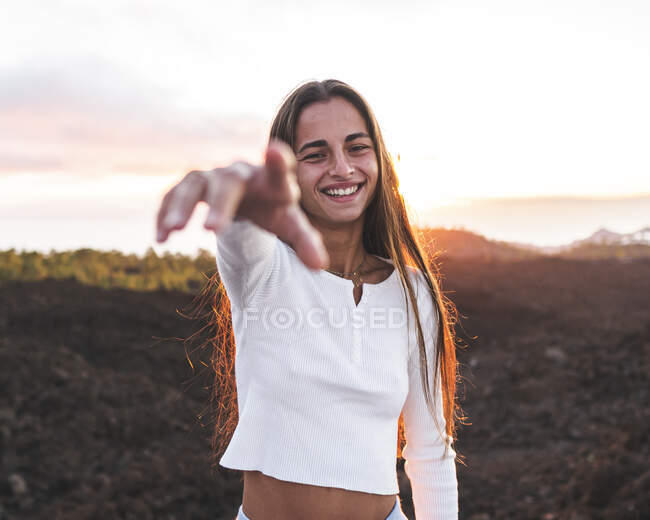 Conteúdo adolescente com braço estendido olhando para a câmera na montagem contra o oceano ao pôr do sol em Tenerife Espanha — Fotografia de Stock