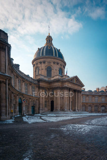 Exterior of College of Four Nations with columns and dome against snowy walkway under cloudy blue sky in Paris France — Stock Photo