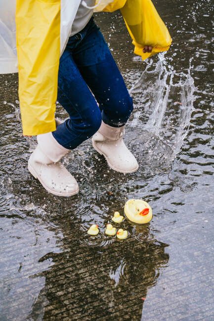 Зверху врожай анонімний дитина в гумових чоботях розважається в калюжі з розбризкуваною акваріумом в дощовий день — стокове фото