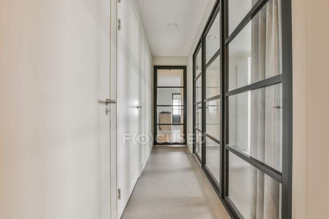 Светлый коридор со стеклянными дверями и белыми стенами в современной квартире с минималистическим стилем — стоковое фото