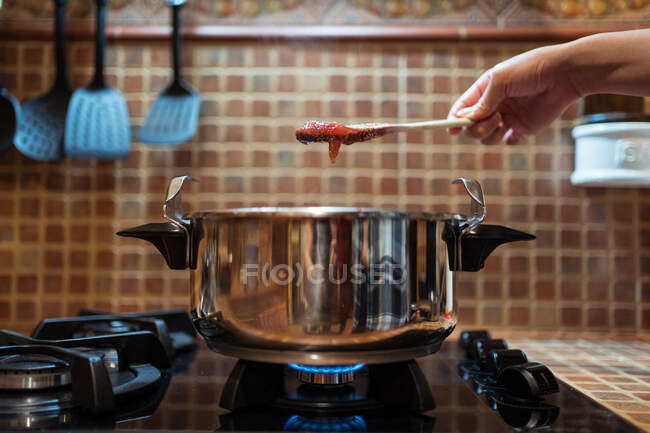 Crop pessoa anônima com deliciosa marmelada de figo na espátula sobre fogão de pressão no fogão a gás na cozinha — Fotografia de Stock