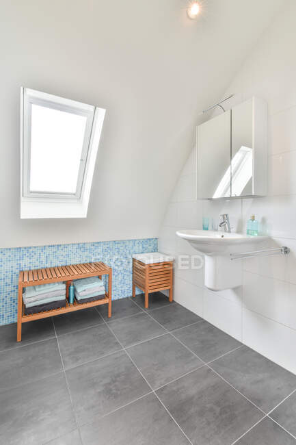 Interior do banheiro contemporâneo com lavatório e janela acima da mesa no piso em azulejos em casa de luz — Fotografia de Stock