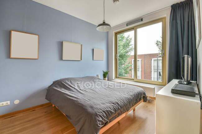 Gray duvet on bed against commode and windows in apartment with lamp and various pictures hung online — Stock Photo