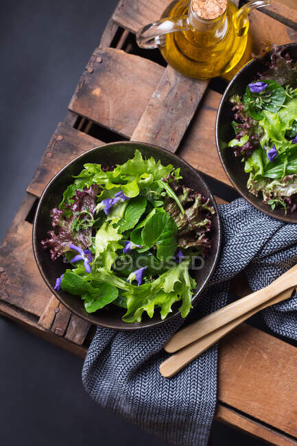 Зверху смачний вегетаріанський салат з зеленим і червоним листям салату і їстівними квітами проти глечика олії — стокове фото