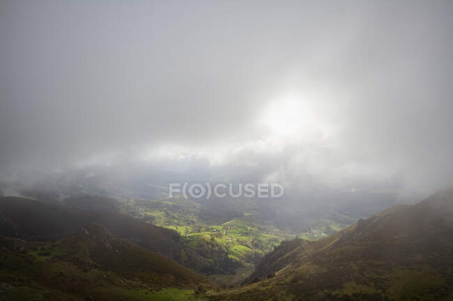 Сверху живописные зеленые холмы и долина под густыми серыми облаками с солнечным светом — стоковое фото