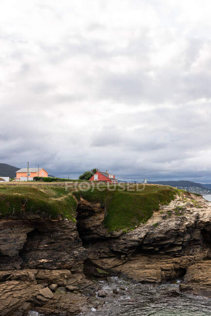 Scenery view of rough shore against mountain with residential building under shiny cloudy sky in sunlight — Stock Photo