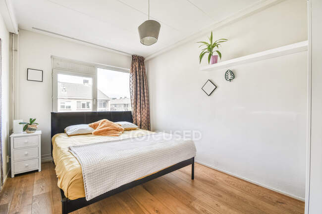 Интерьер уютной спальни с горшечным растением и кроватью расположен возле окна в современном коттедже — стоковое фото