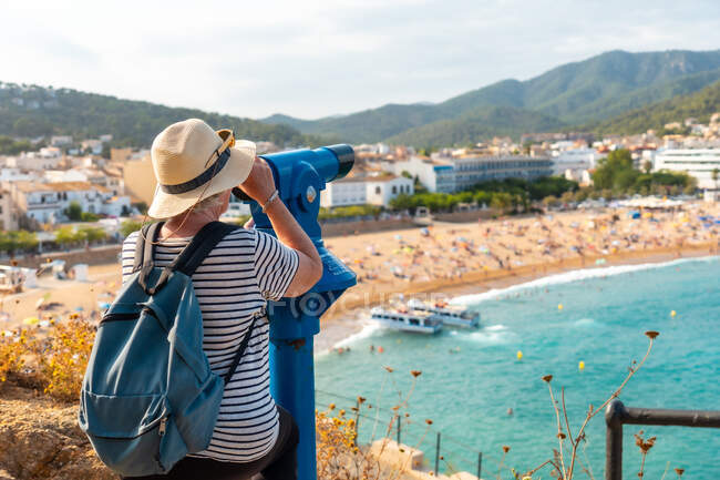 Vista lateral del turista senior con mochila observando el mar en el mirador con prismáticos - foto de stock