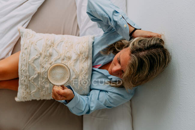 From above female in shirt with cup of aromatic coffee looking away at home — Stock Photo