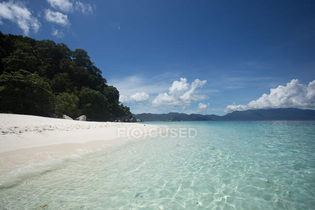 Pintoresca vista de mar azul cristalino lavado playa de arena rodeada de colinas - foto de stock