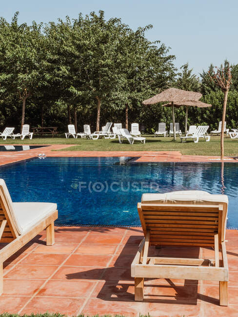 Chaises longues confortables placées près de la piscine avec de l'eau bleue par une journée ensoleillée dans la cour de la station — Photo de stock