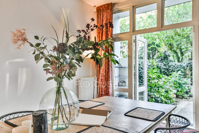 Interno della sala da pranzo con tavolo in legno decorato con fiori in vaso di vetro in casa moderna — Foto stock
