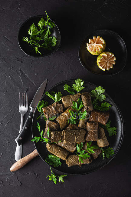 Von oben schmackhaftes Sarma mit Petersilie Zitrone und Gabel und Messer auf dunklem Hintergrund — Stockfoto