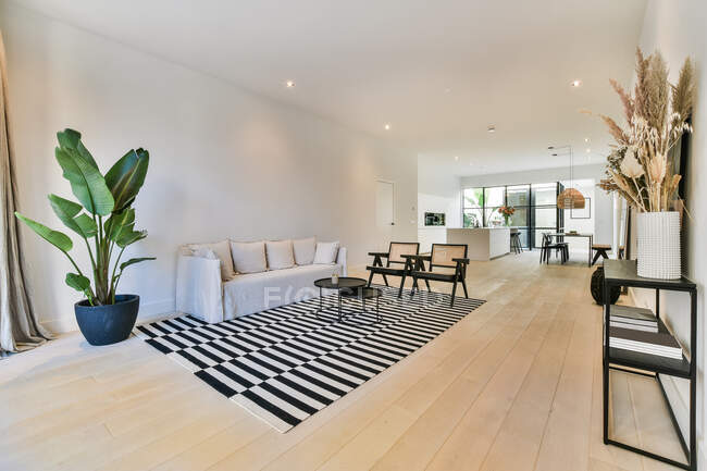 Интерьер современной комнаты с диваном и креслами на ковре с полосатым орнаментом на паркете в доме — стоковое фото