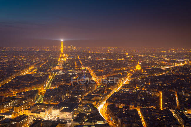 Вид с воздуха на темное ночное небо над освещенными зданиями и дорогами с высокой Эйфелевой башней в районе Парижа — стоковое фото