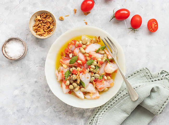 Salada de tomate e bacalhau com muito azeite em um prato fundo com garfo e uma tigela de cebola frita — Fotografia de Stock