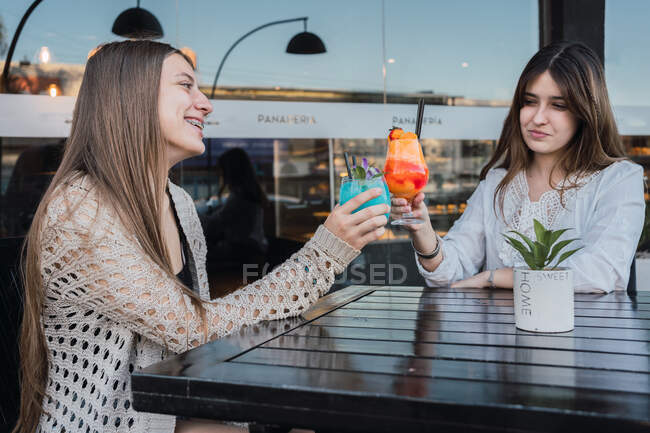 Весела жінка-підліток взаємодіє під час клонування келихів смачних освіжаючих напоїв за столом у міських кафетеріях — стокове фото