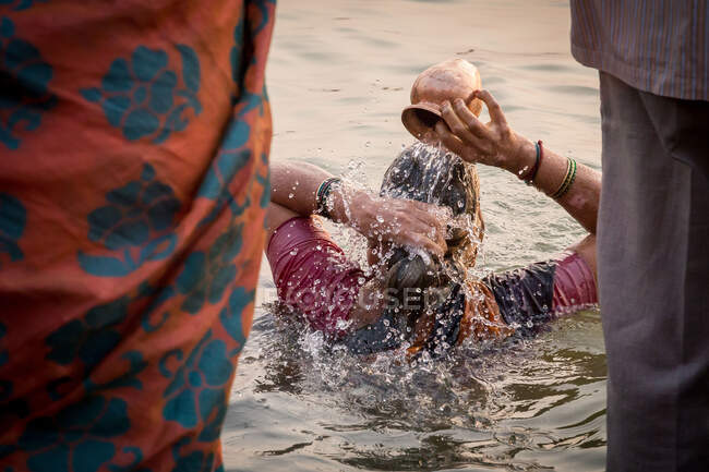 Nepal - 27 de novembro de 2015: Visão traseira da mulher molhada étnica sem rosto derramando água na cabeça durante a lavagem sagrada na água suja do rio no Nepal — Fotografia de Stock