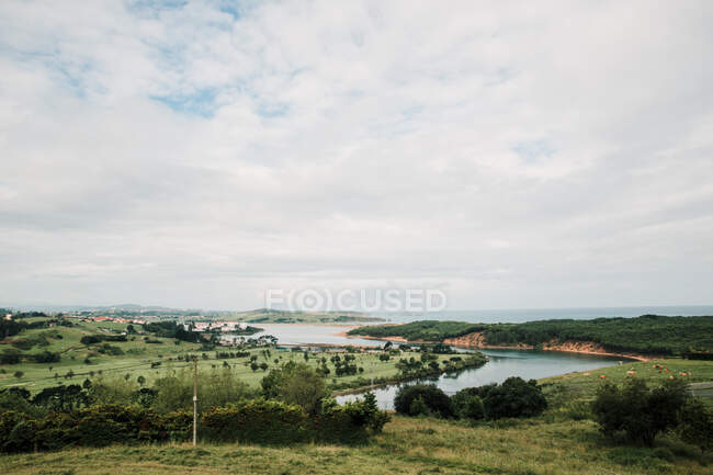 Pittoresca vista di prati con alberi lussureggianti e colline contro l'oceano infinito sotto il cielo nuvoloso nella campagna della Cantabria Spagna — Foto stock
