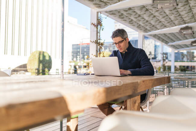 Young male in trendy outfit browsing netbook while working on project on street — Stock Photo