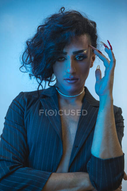 Young transsexual male model with makeup in stylish jacket looking at camera on blue background — Stock Photo