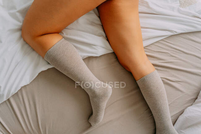 Ritaglio femminile irriconoscibile in calzini ginocchio sdraiato su lenzuolo accartocciato — Foto stock