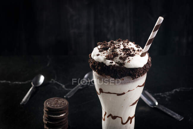 Вкусный молочный коктейль с измельченным печеньем и соломой в стакане с шоколадным соусом — стоковое фото